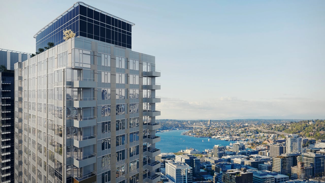 Modern high-rise apartment building with glass facade and balconies, overlooking a city and bay.