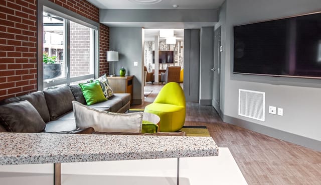 Modern lounge area with a comfortable sectional sofa, vibrant green accent chair, and a large television on the wall.