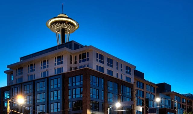 Modern apartment building with the Space Needle in the background at dusk.