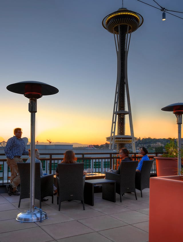 Rooftop deck with Space Needle view and people relaxing at sunset.