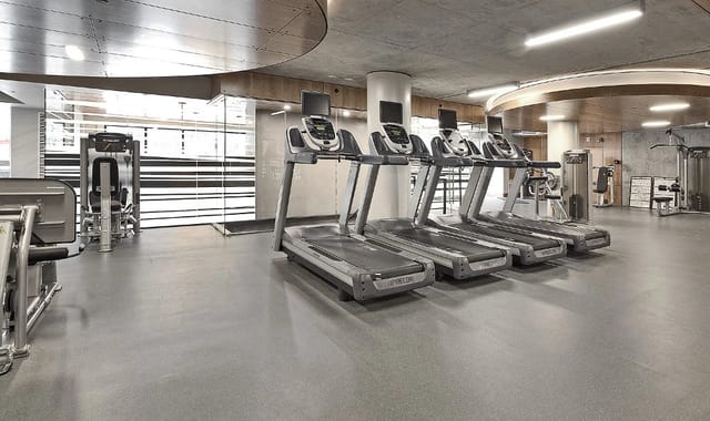 Row of treadmills in a modern apartment gym with weight machines visible in background.