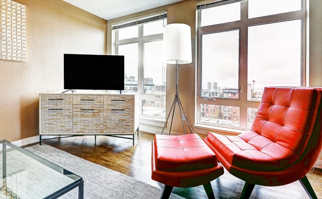 Living room with a modern TV console, red armchair, and floor-to-ceiling windows.