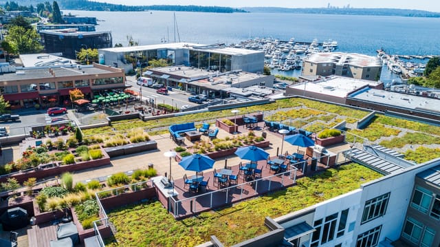 Rooftop lounge area with seating, tables, umbrellas, and a grill, overlooking a marina and bay.