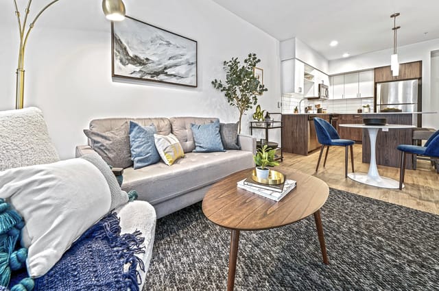 Modern living room with sofa, coffee table, and view of kitchen with dining area.