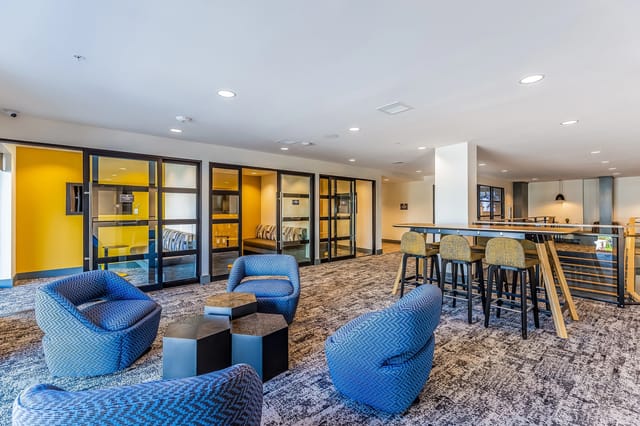 Modern lounge area with blue armchairs, hexagonal coffee tables, and a high-top bar with stools.