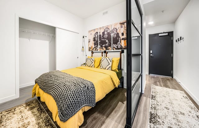 Bedroom with yellow bedding, grey throw blanket, and modern art.