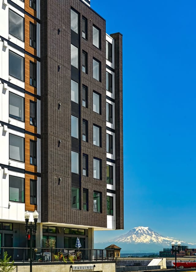 Modern apartment building exterior with brick and white facade, overlooking a snow-capped mountain.
