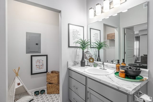 Modern bathroom vanity with marble countertop, dual sinks, and ample storage. Includes decorative items and a large mirror.