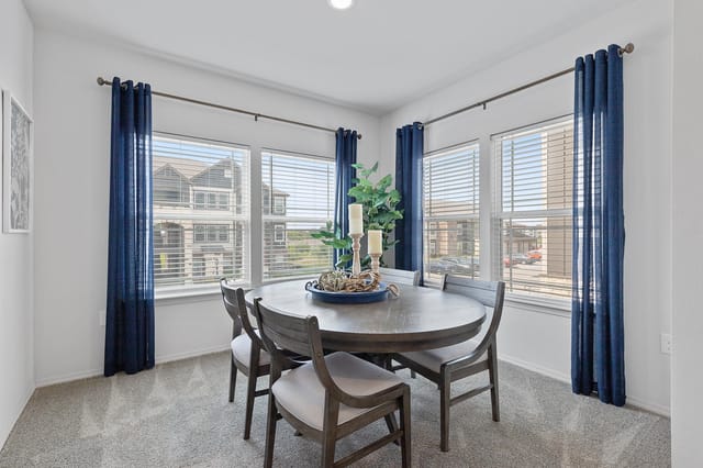 Dining room with a round table and four chairs, featuring blue curtains and a view of the exterior buildings.