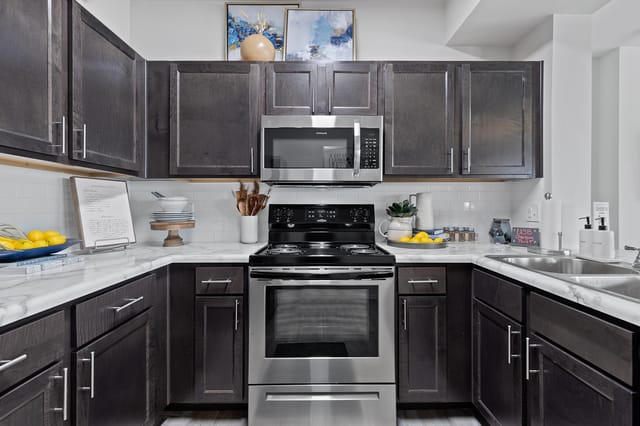 Modern dark wood U-shaped kitchen with stainless steel appliances, white subway tile backsplash, and marble countertops.
