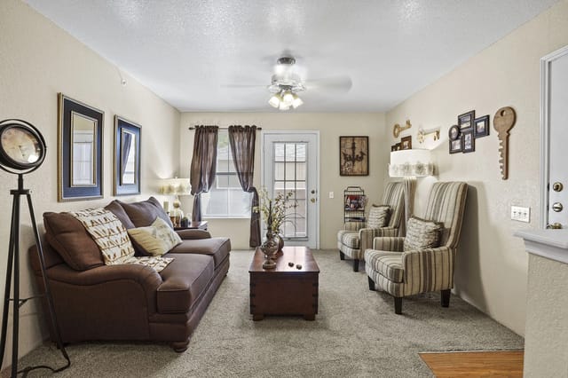 Living room in an apartment with a brown sofa, striped armchairs, a coffee table, and dark curtains.