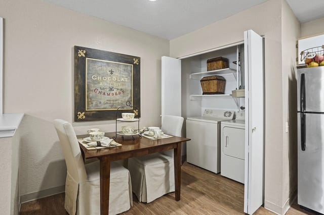 Dining table with four slipcovered chairs beside a laundry closet housing a washer and dryer.