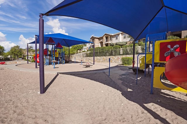 Playground area with slides, swings, and a see-saw under blue canopies.