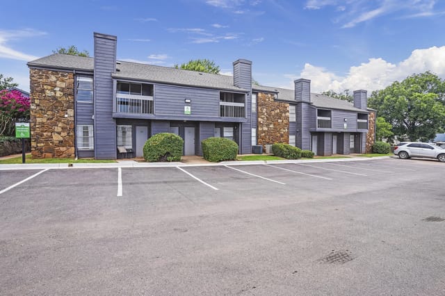 Exterior view of a blue, stone-accent apartment building with parking lot.