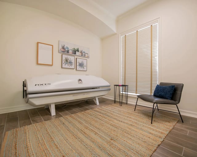 A room with a white massage bed and a chair with a blue pillow.