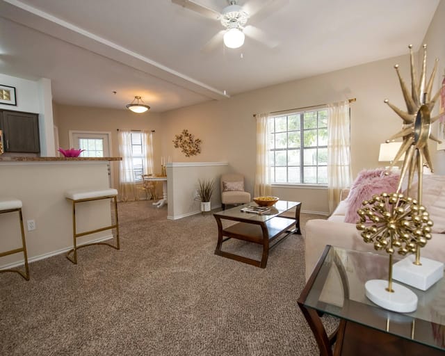 A living room with a brown carpet and a glass coffee table.