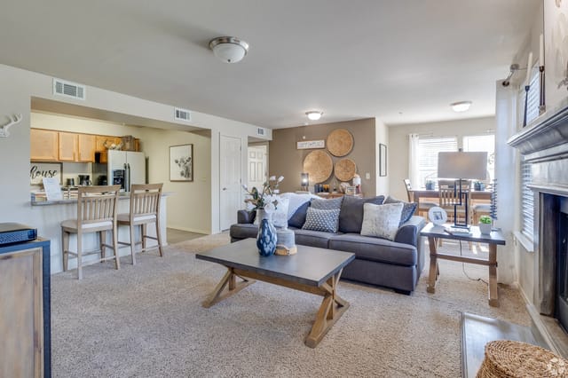 Open-concept living room with gray sofa, coffee table, kitchen counter with stools, and dining area.