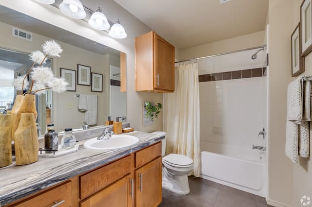 Bathroom in an apartment with a wooden vanity, large mirror, and a shower-tub combo.