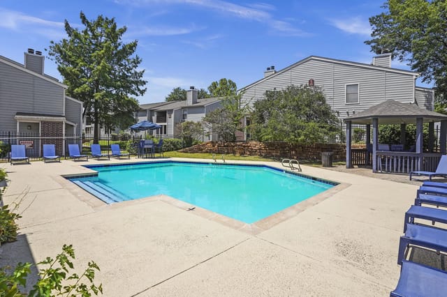 A swimming pool surrounded by a concrete patio and blue lounge chairs.