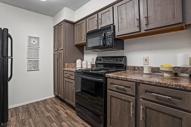 Modern kitchen with dark wood cabinets, black appliances, and granite countertops.