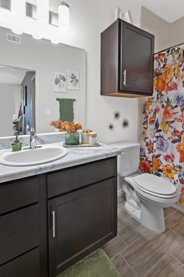 A bathroom with a floral shower curtain and a white toilet.