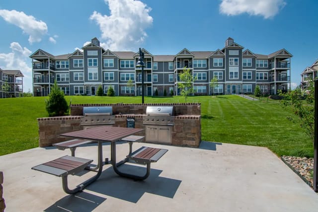 Outdoor communal grilling station with a picnic table in front of a multi-building apartment complex.