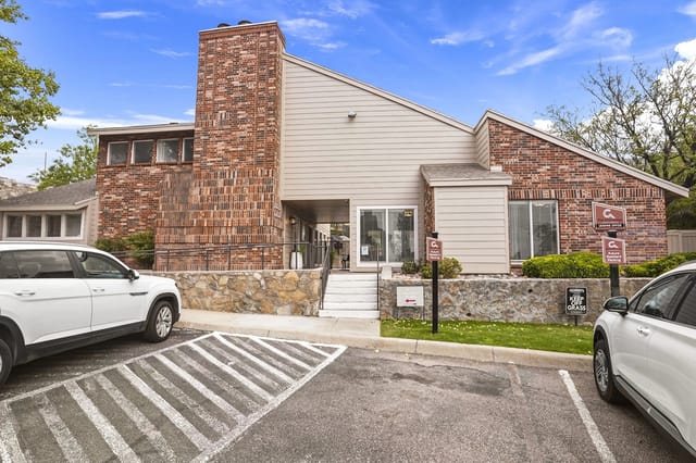 Exterior view of a brick apartment building entrance with a stone base and cars parked nearby.