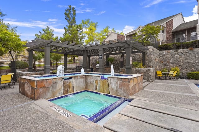Outdoor pool area with a stone fountain, seating, and a pergola at a residential community.
