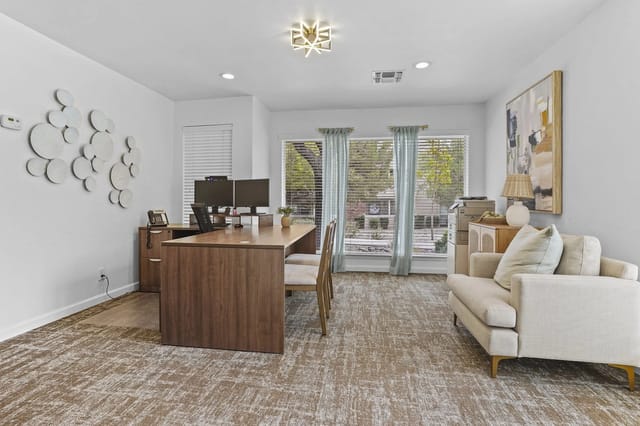 Office area with a wooden desk, two monitors, and a beige sofa by large windows.