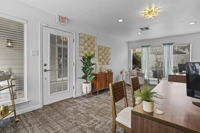 Interior community lounge with a long table, chairs, decor, and an exit door.