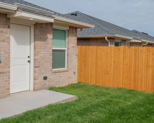 Exterior view of a brick building with a white door and a wooden fence.