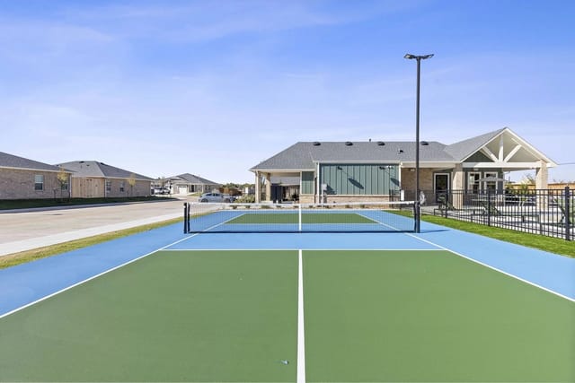 Tennis court with blue and green surfaces and a net, with buildings in the background.