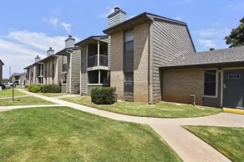 Exterior view of apartment buildings with brick and siding, walkways, and manicured lawns.