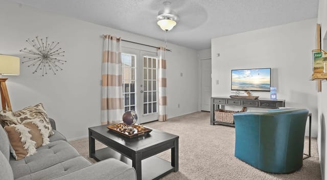 Living room with gray sofa, teal armchair, coffee table, TV, and ceiling fan.
