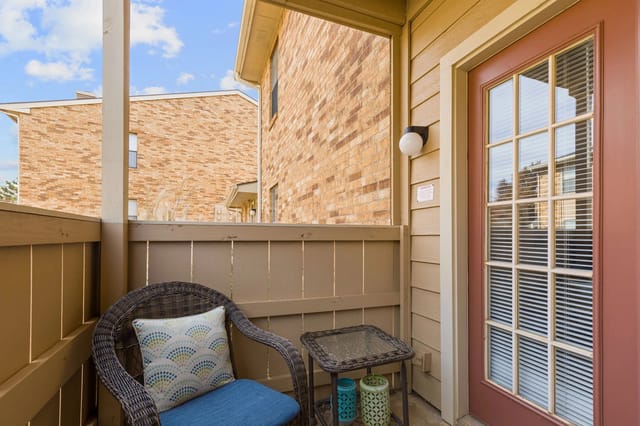 Balcony with a wicker chair and table overlooking brick buildings.