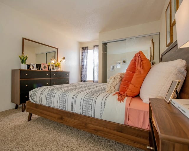 Stylish bedroom with a wooden bed frame, patterned bedding, and a dresser with a mirror.