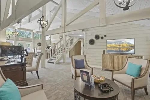 Bright communal lounge with couches, chairs, a staircase, and wall decor.