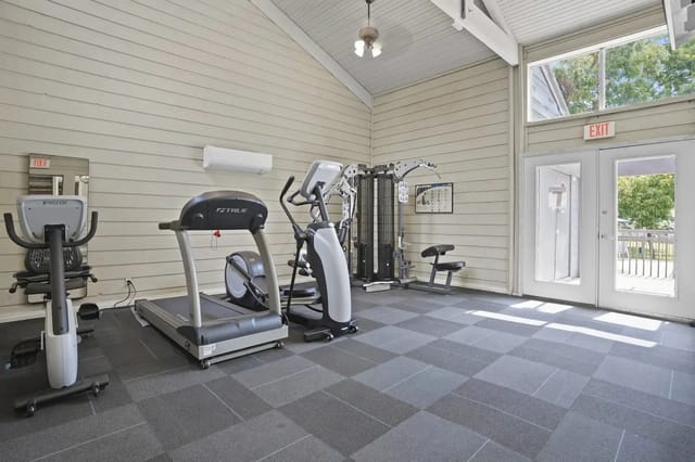 Indoor community gym with treadmills, elliptical, weight stack, and an exit door.