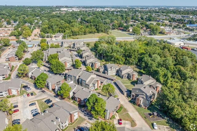 Aerial view of a multifamily property with multiple buildings, parking lots, and lush green trees.