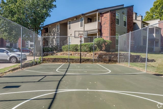 Outdoor basketball court with a chain-link fence and apartment buildings in the background.