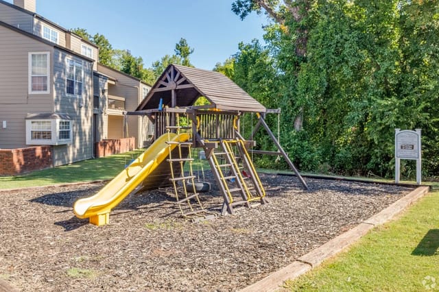Playground with slide, swings, and climbing ladder next to apartment buildings.