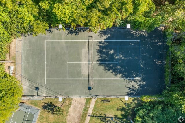 Aerial view of a tennis court with trees and shadows.