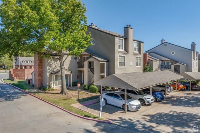 Apartment building exterior with covered parking and mature trees.