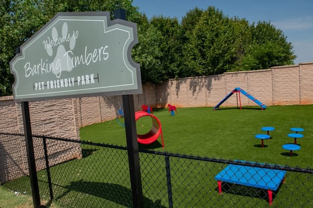 Sign reads 'Welcome to Barking Timbers Pet Friendly Park' near a fenced playground.