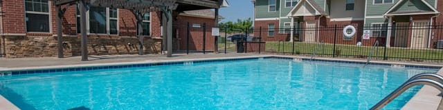 Outdoor apartment pool with a concrete deck and black metal fence.