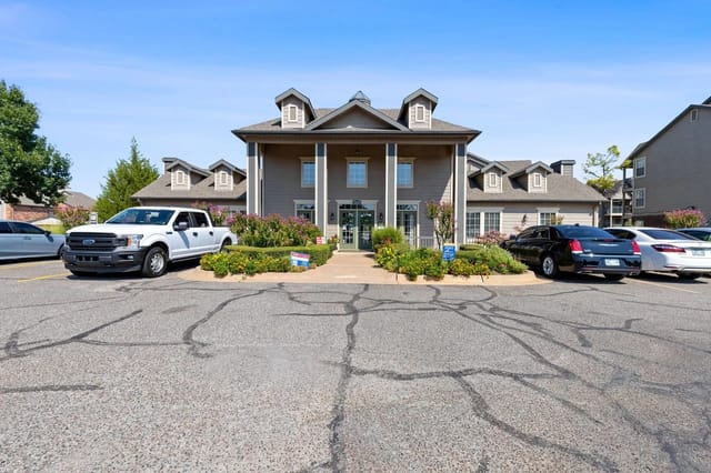 Front entrance of apartment building with parking lot and cars.