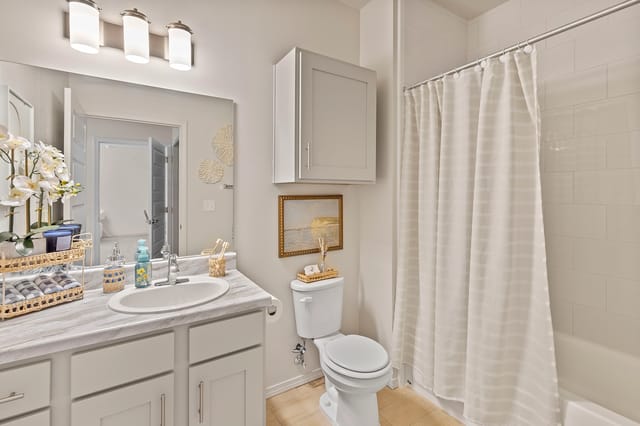A modern bathroom with a marble vanity, toilet, and bathtub with a white shower curtain.