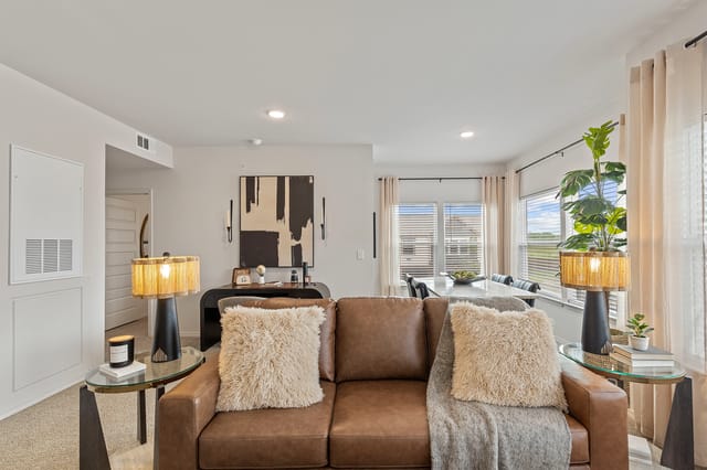 Interior of a modern living room with a brown leather sofa, throw pillows, and a coffee table with a candle.