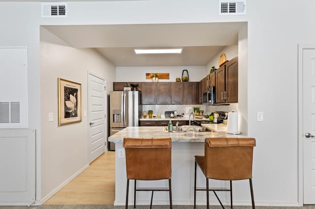 Modern kitchen with granite countertops, stainless steel appliances, and breakfast bar with leather stools.