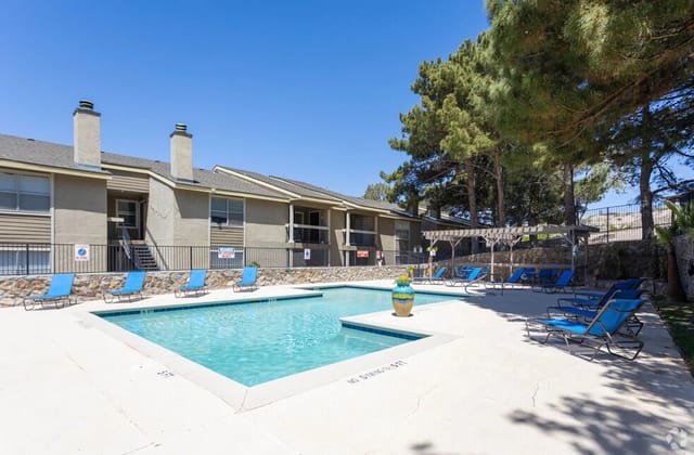 Outdoor swimming pool with lounge chairs and surrounding apartment buildings on a sunny day.